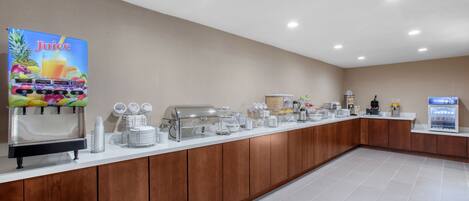 A buffet setup with a juice station, coffee makers, and a refrigerator.
