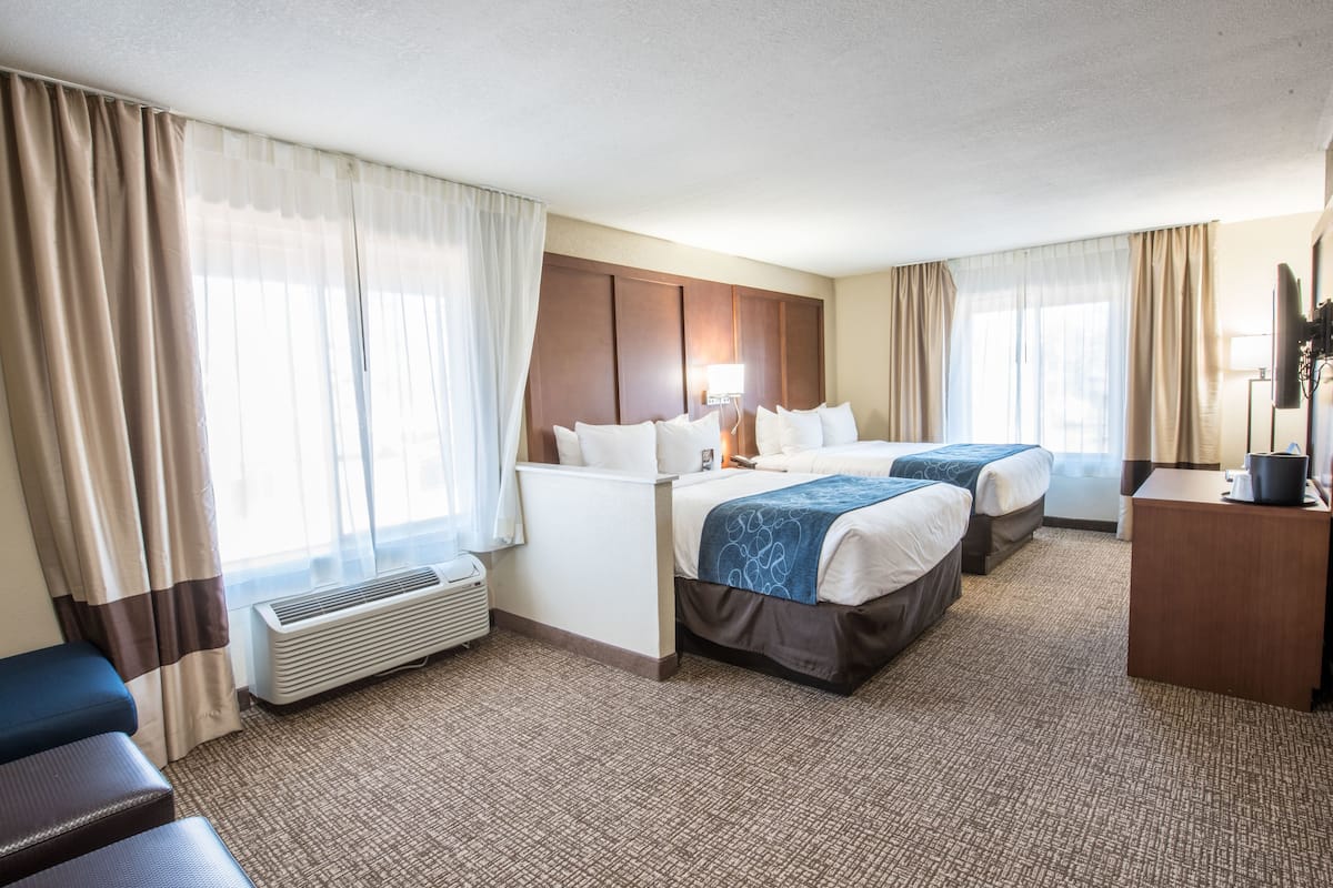 Habitación de hotel con dos camas, un escritorio, una silla y un amplio ventanal con cortinas.
