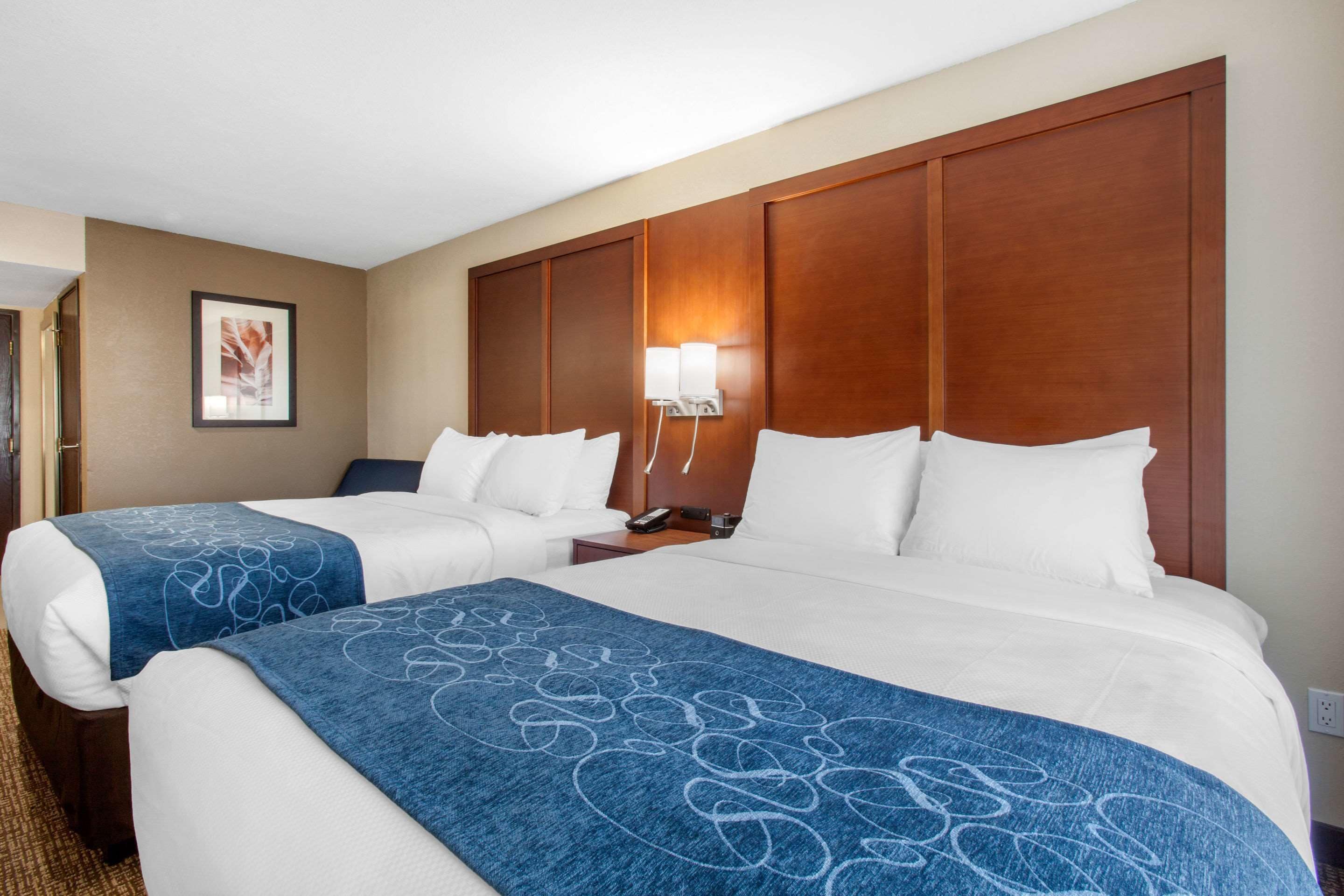 A hotel room with two beds, a wooden headboard, a nightstand, a lamp, and a framed picture on the wall.