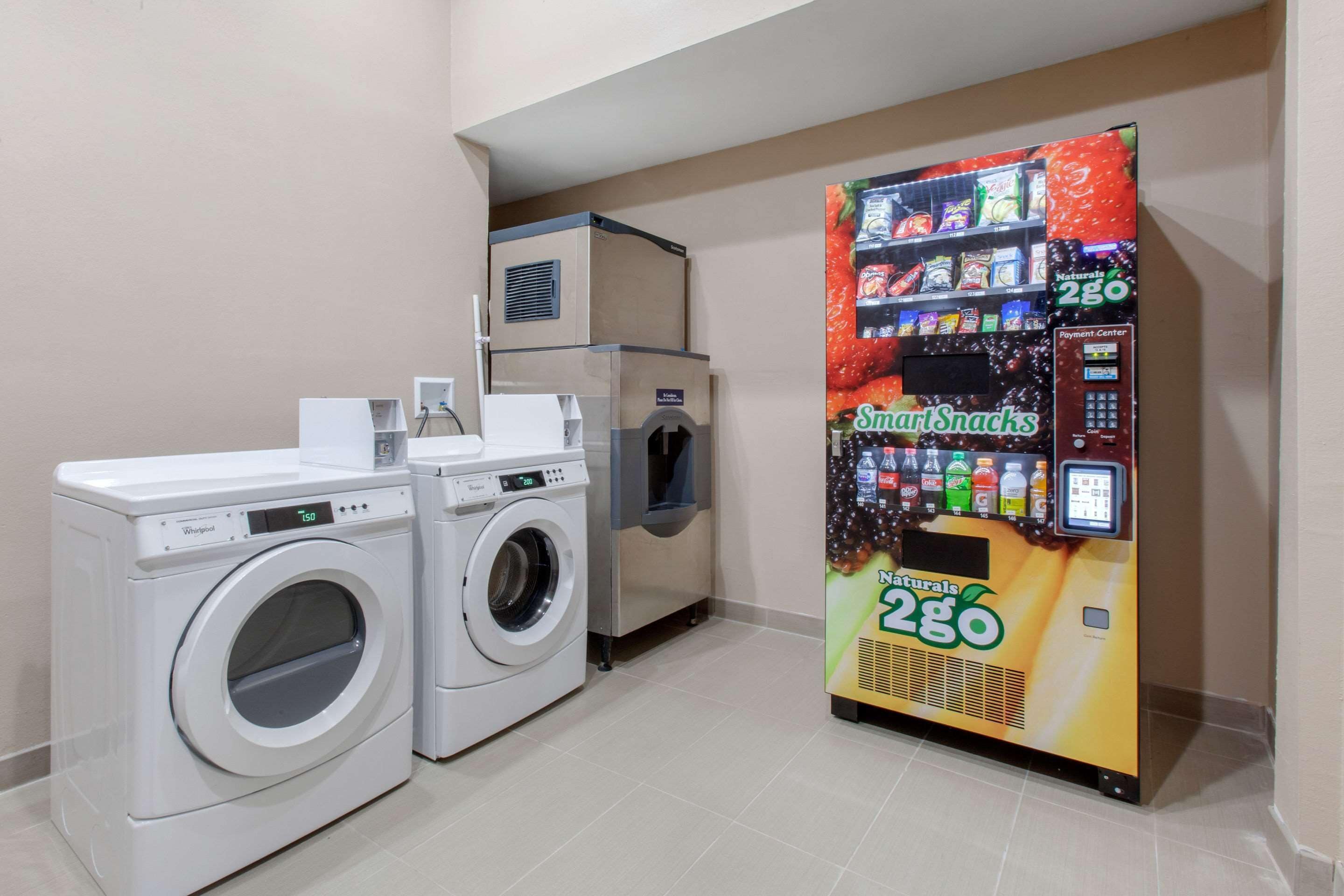 Ett tvättrum med en tvättmaskin och en torktumlare från Whirlpool, en vattenautomat och en försäljningsautomat som säljer SmartSnacks.