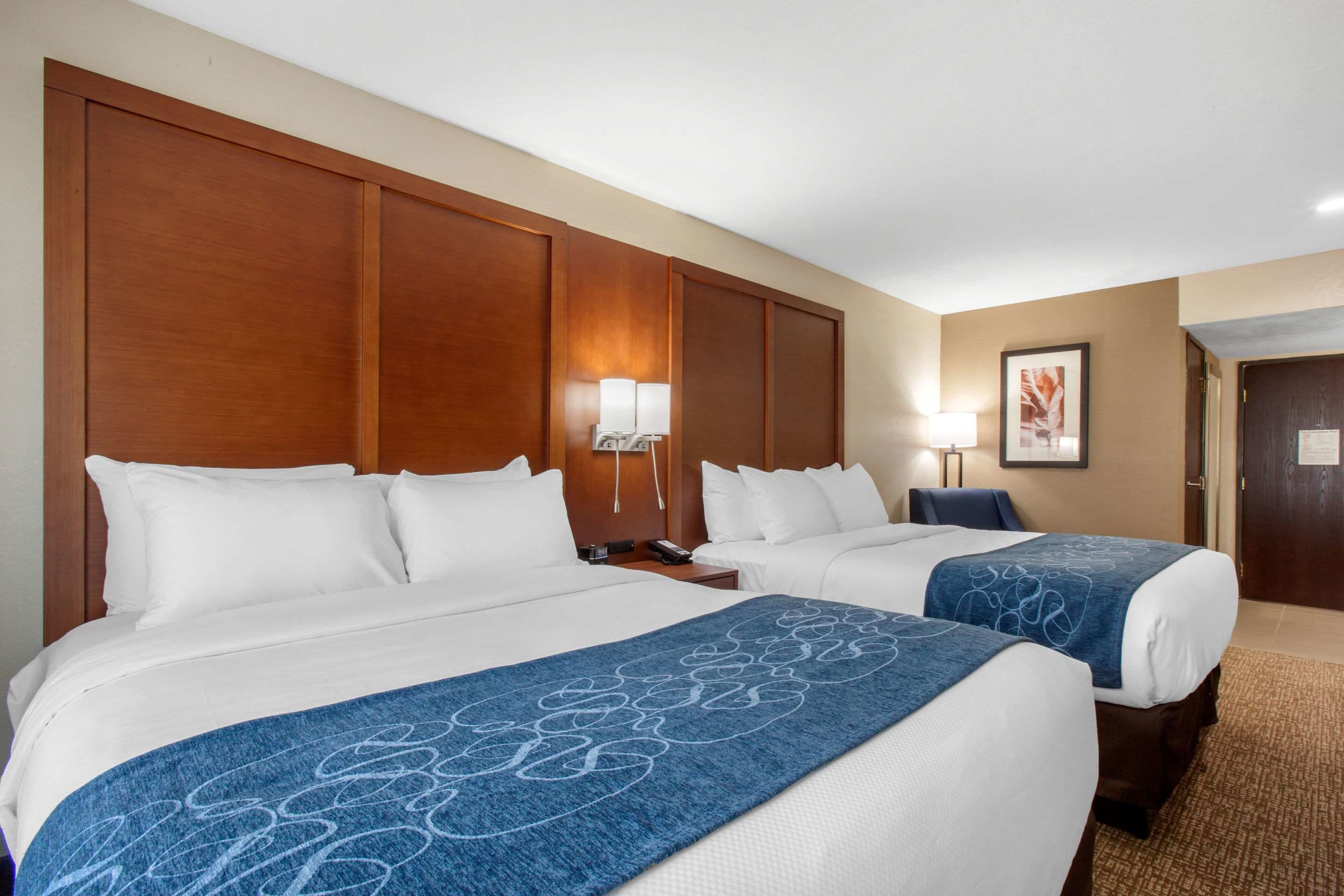 A hotel room with two beds, a wooden headboard, a nightstand with a lamp, and a framed picture on the wall.