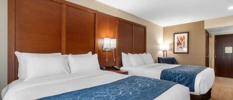A hotel room with two beds, a wooden headboard, a nightstand with a lamp, and a framed picture on the wall.