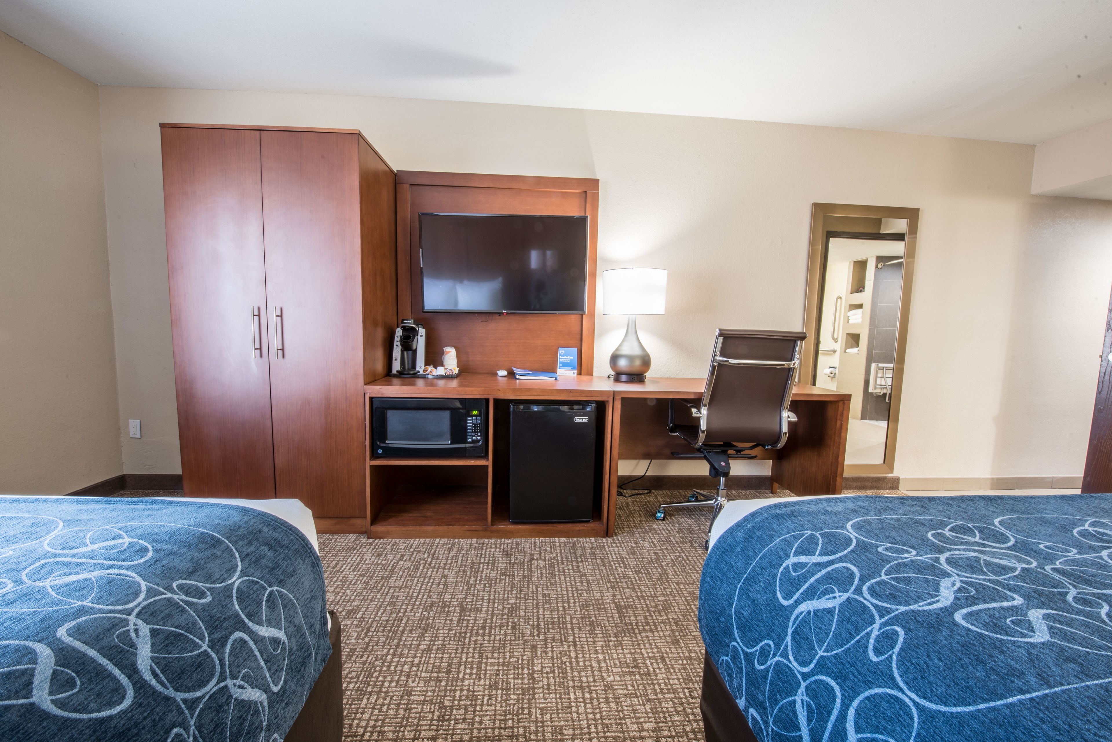A hotel room with two beds, a desk with a computer, a microwave, a coffee maker, and a TV.