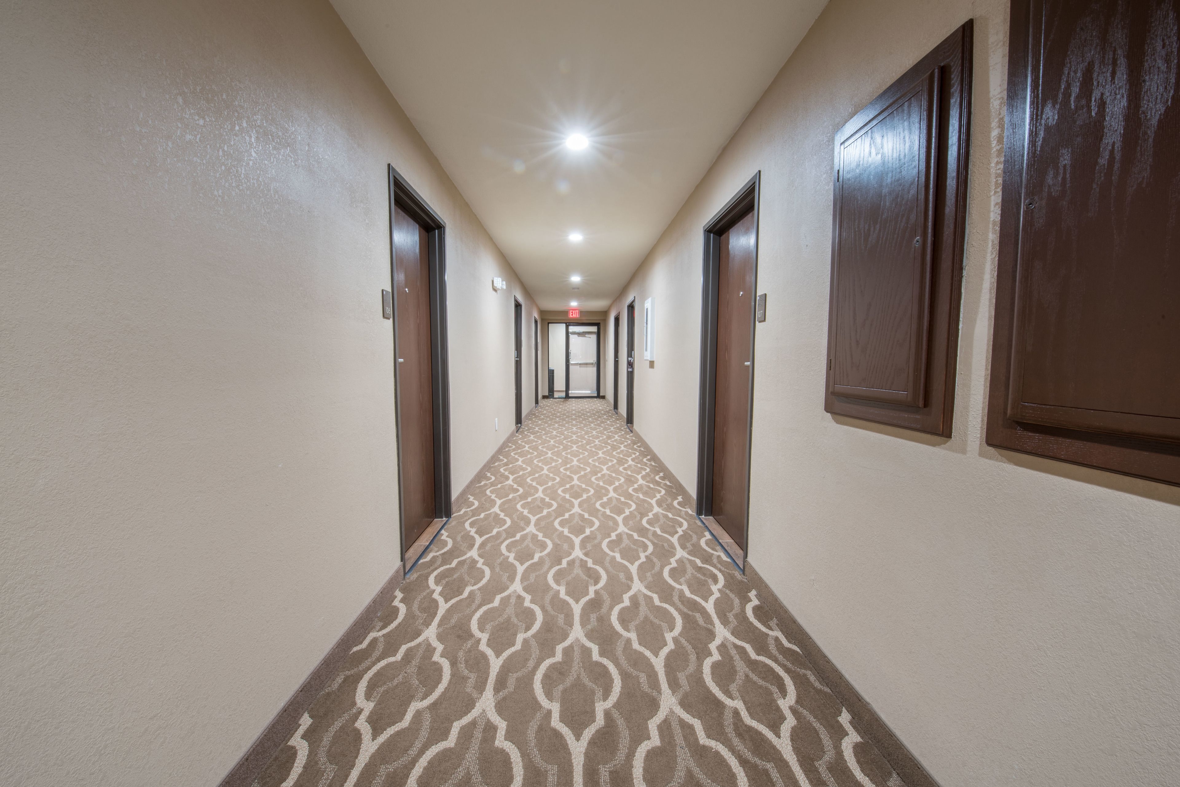 A hotel hallway with patterned carpet, wooden doors, and a ceiling light.