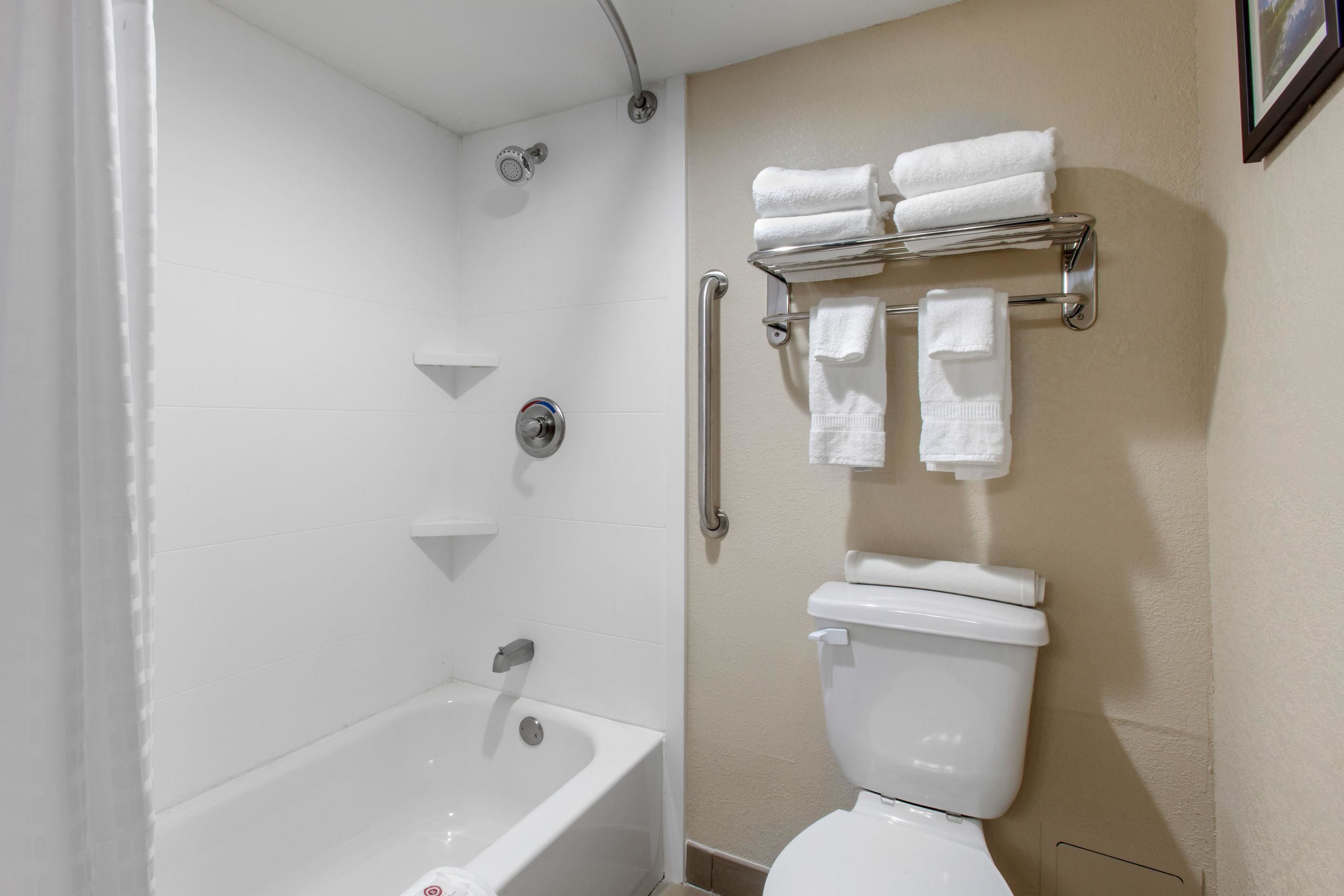 Un baño con bañera, inodoro y barras de apoyo.