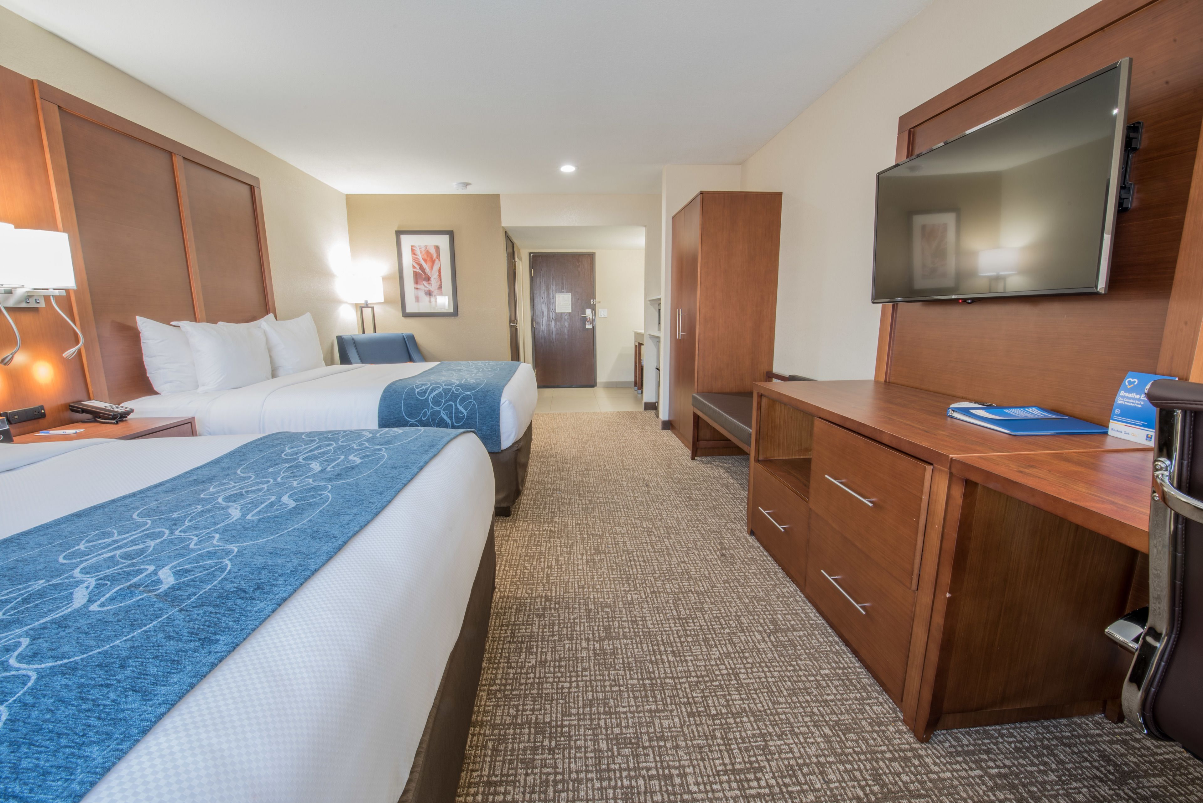 A hotel room with two beds, a desk, a TV, and a wardrobe.