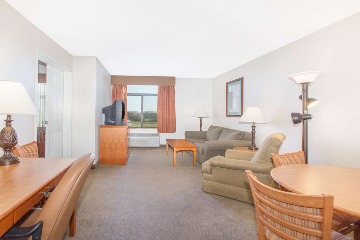 A hotel room with a dining table, a sofa, a TV, and a window with curtains.