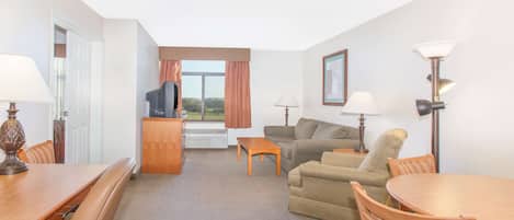 Habitación de hotel con una mesa de comedor, un sofá, un televisor y una ventana con cortinas.