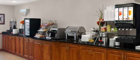 Zona de recepción de hotel con una larga barra de mostrador, una máquina de café, un refrigerador y una vitrina con productos alimenticios.
