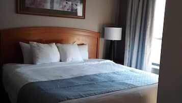 Ein Hotelzimmer mit einem großen Bett, einem Kopfteil, einem Gemälde an der Wand, einer Lampe und einem Fenster mit Vorhängen.