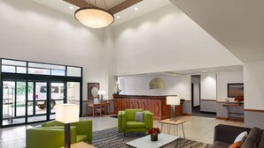 A spacious lobby with a reception desk, green seating, and a modern chandelier. - Wingate by Wyndham Bentonville AR (Bentonville)
