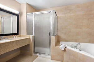Un baño moderno con encimera de granito, cabina de ducha con paredes de vidrio y bañera blanca.