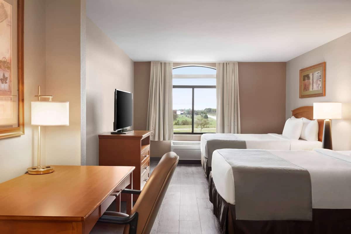 A hotel room with two beds, a desk with a chair, a television, and a window with curtains.
