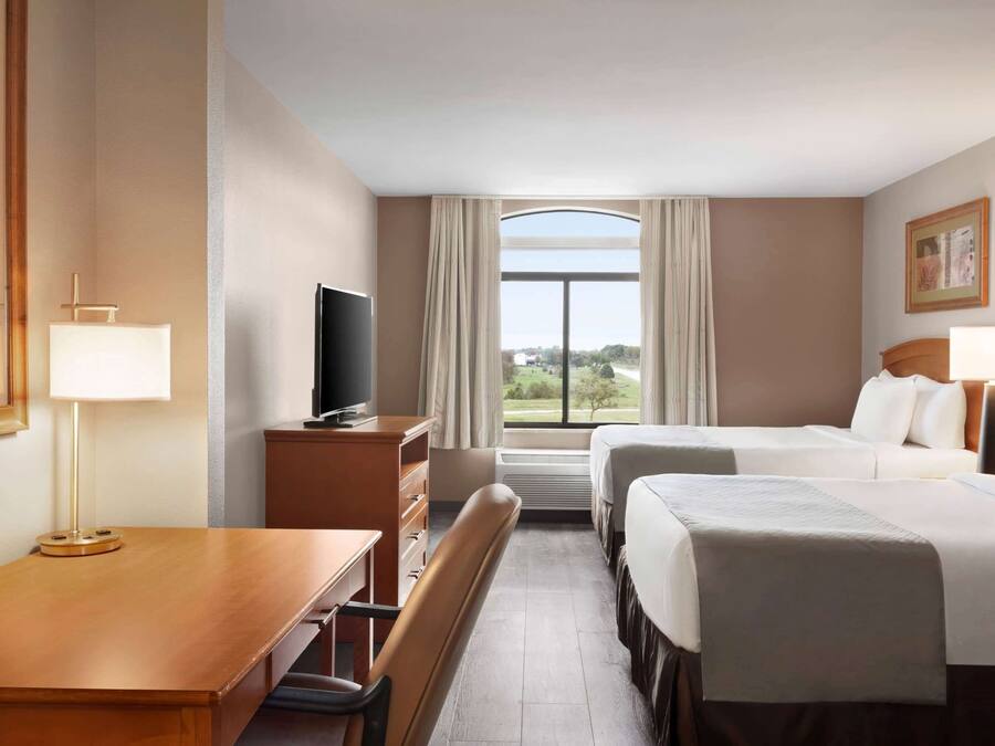 Quarto de hotel com duas camas, uma escrivaninha com cadeira, televisão e janela com cortinas.