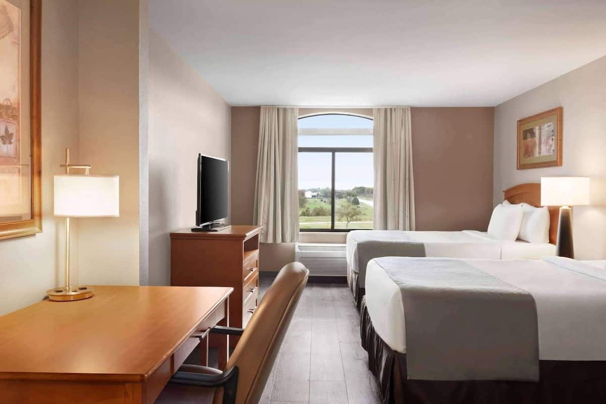 A hotel room with a desk, two beds, a TV, and a large window with curtains.