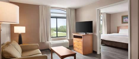 Habitación de hotel con cama, televisión, escritorio, silla, lámpara y ventana con cortinas.