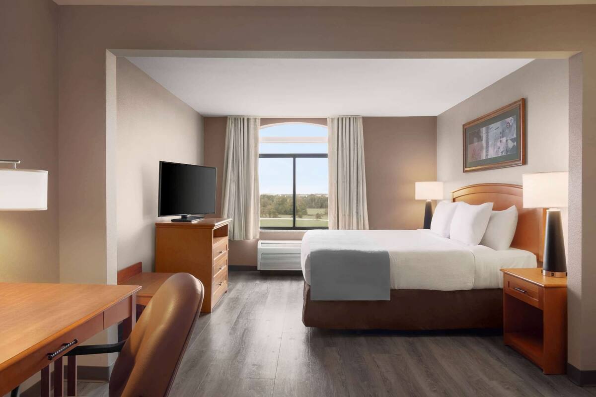 A hotel room with a bed, a desk, a television, and a window with curtains.