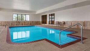 An indoor swimming pool with clear blue water, a tiled border, and a seating area with chairs and a table. - Wingate by Wyndham Bentonville AR (Bentonville)