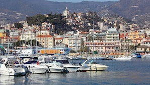 A marina with boats docked, a coastal town with colorful buildings, and a hill with a church in the background. - Pollon Inn Sanremo (Sanremo)