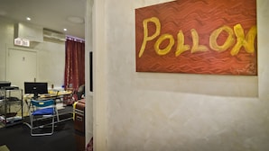 A room with a large painting of the word "POLLON" on the wall, a desk with a computer, a chair, and a small table with a lamp. - Pollon Inn Sanremo (Sanremo)