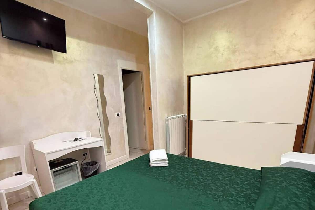 Habitación de hotel con una cama grande, un escritorio, una silla, un televisor montado en la pared y un radiador.