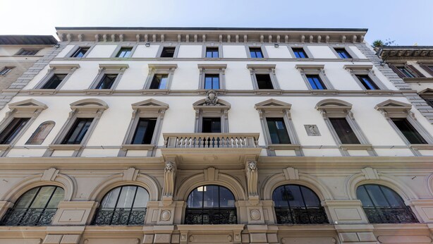 Ein mehrstöckiges Gebäude mit klassischer Architektur, gekennzeichnet durch Rundbogenfenster und dekorative Stuckleisten.