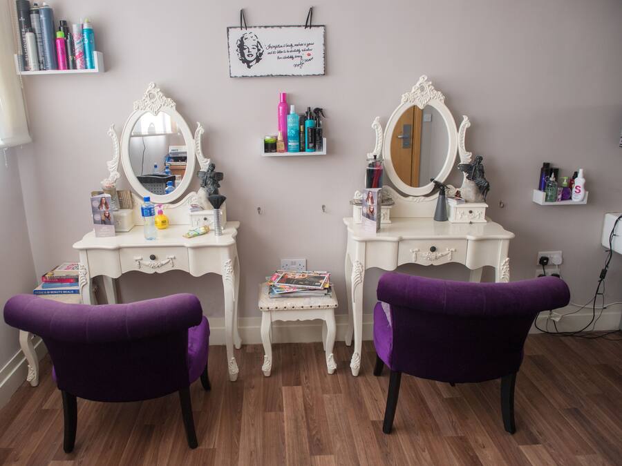 Een opbergruimte voor toiletartikelen met twee spiegels, paarse stoelen en planken.