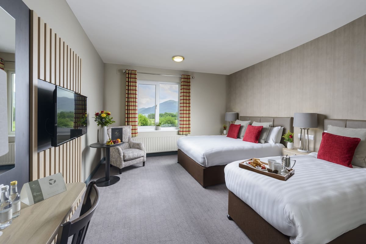 Habitación de hotel con dos camas, un escritorio, un televisor y una ventana con cortinas.