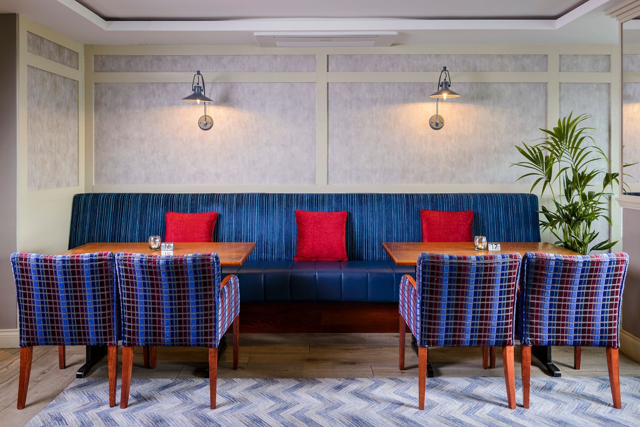 Un coin repas avec un banc bleu rembourré, des chaises à carreaux et deux lampes fixées au mur.