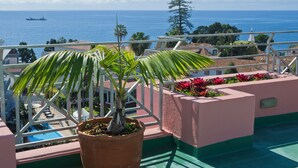 A balcony with a potted plant, a pool, and a view of the sea and a ship.