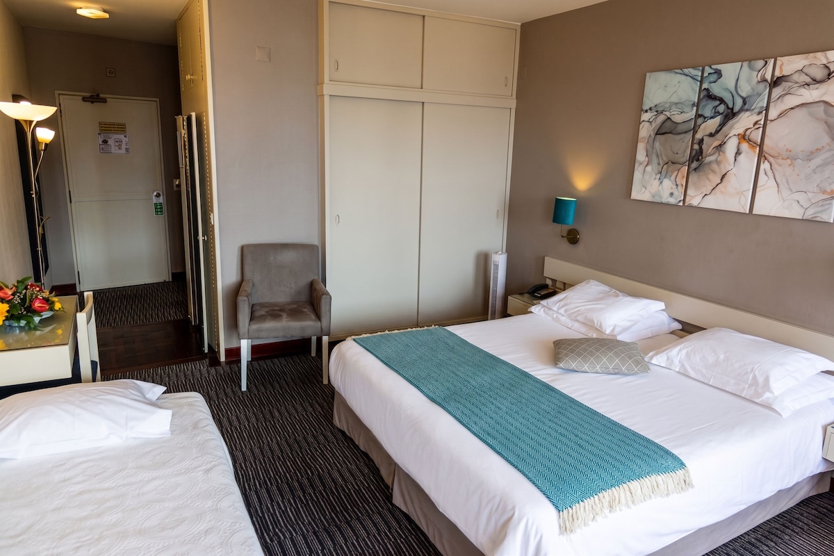 A hotel room with a bed, a chair, a desk with a lamp, and a painting on the wall.