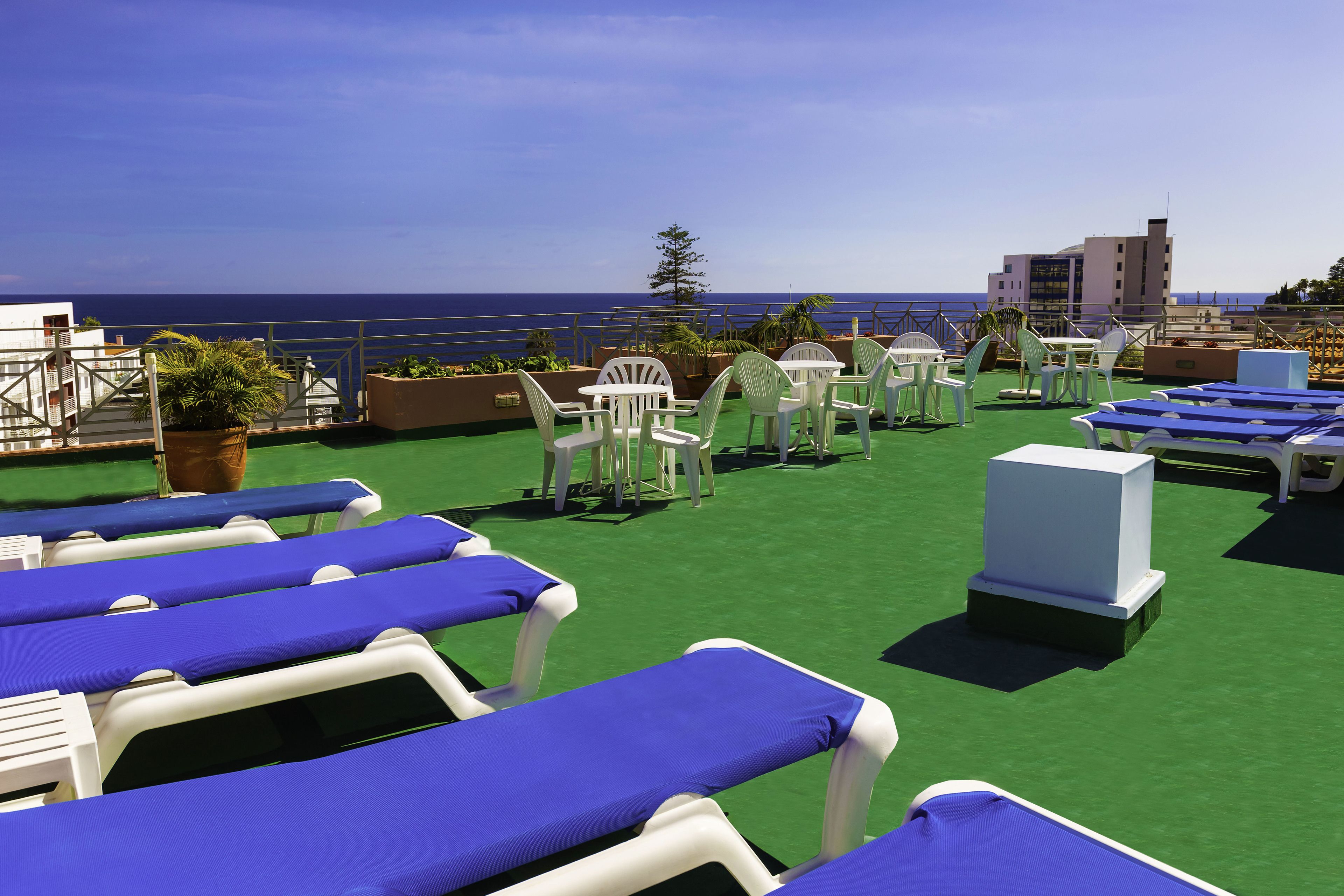 Une terrasse sur le toit, dotée de chaises longues et de tables, recouverte d’une moquette verte, et offrant une vue sur la mer.