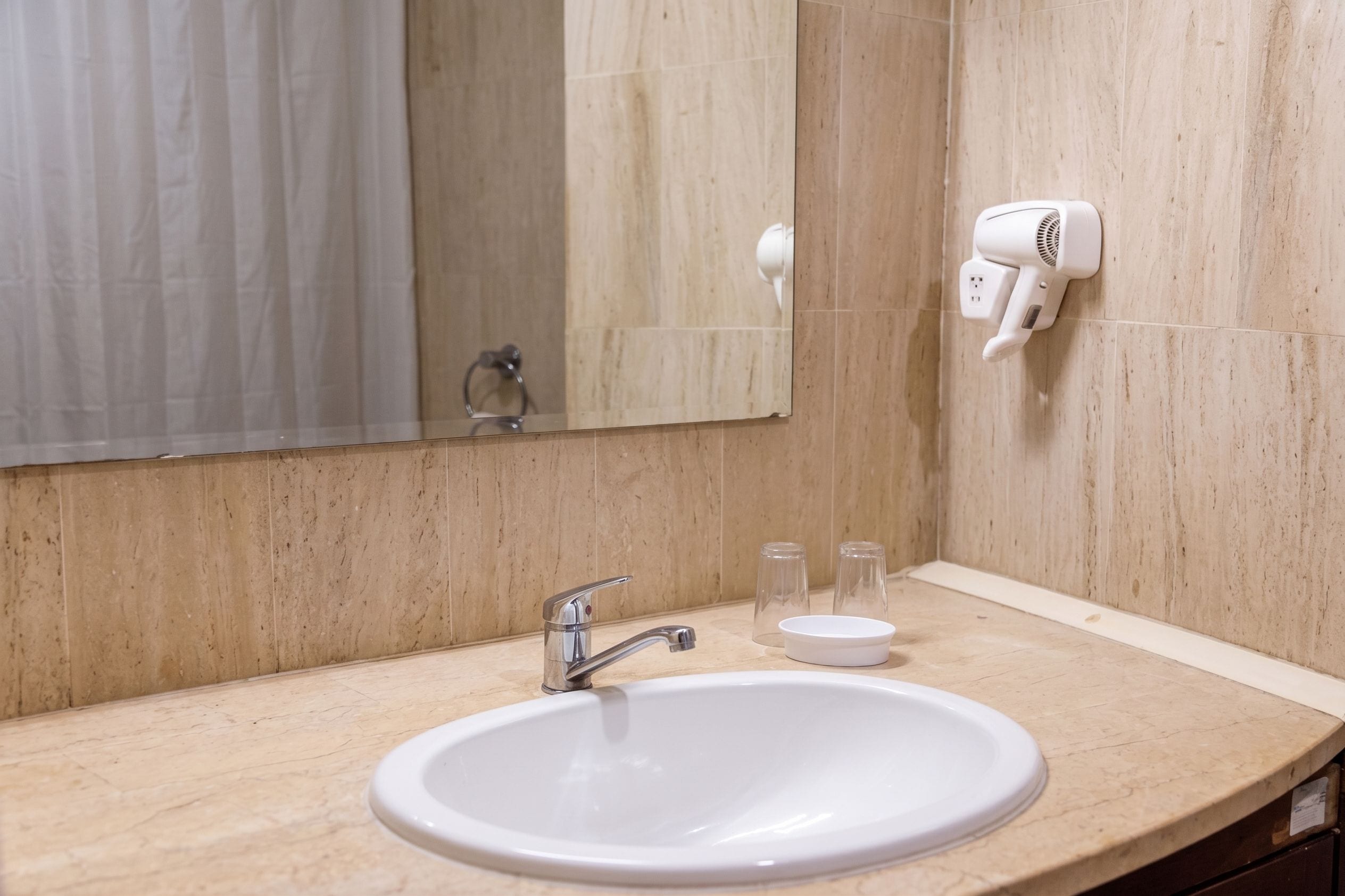 Un baño con lavamanos, espejo, secador de pelo y dos vasos pequeños en la encimera.