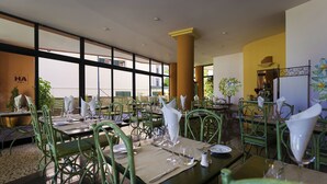 A restaurant with green metal chairs, tables set with white napkins, and large windows offering a view of the outside.