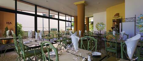 A restaurant with green metal chairs, tables set with white napkins, and large windows offering a view of the outside.