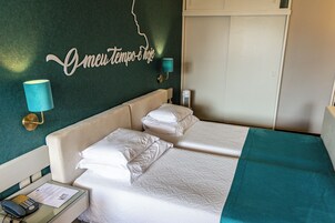 A hotel room with a bed, a nightstand, a lamp, and a wall with a decorative sign.