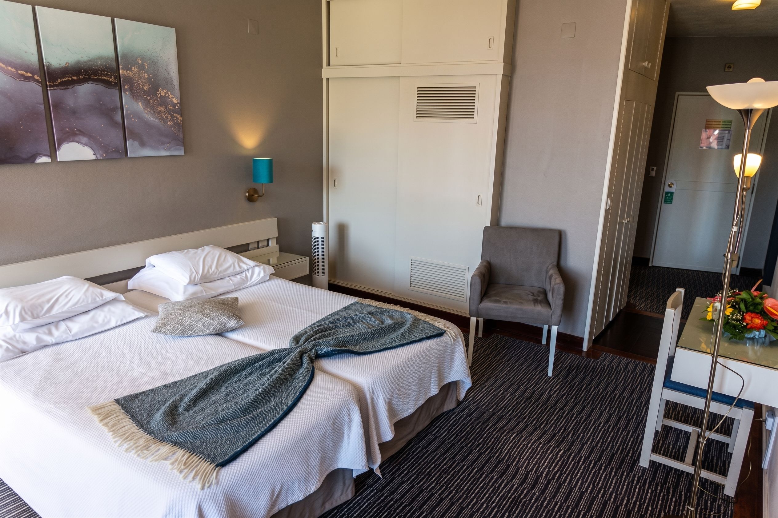 A hotel room with a bed, a chair, a desk, and a wall-mounted air conditioner.