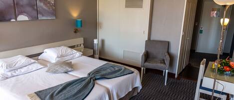 A hotel room with a bed, a chair, a desk, and a wall-mounted air conditioner.