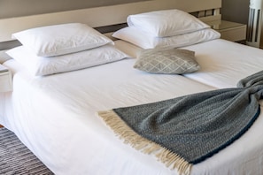 Una cama bien tendida con sábanas blancas y una manta gris estampada.