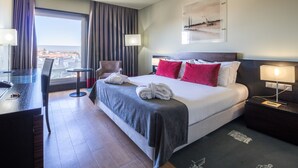 A hotel room with a large bed, a desk, a chair, and a view of the city through the window.