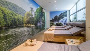 Een spa-ruimte met een riviermuur, massagetafels en uitzicht op een waterval.