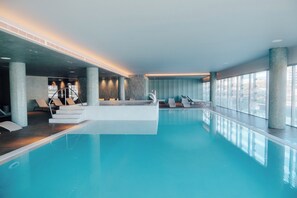 An indoor swimming pool with clear blue water, lounge chairs, and a staircase leading to upper levels.