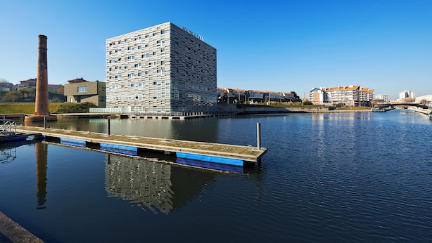 A modern hotel with a unique geometric facade, a dock, and a calm river.