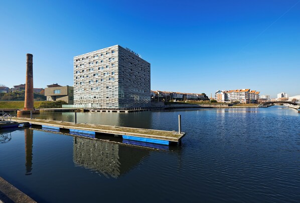 Un hotel moderno con una fachada geométrica única, un embarcadero y un río tranquilo.