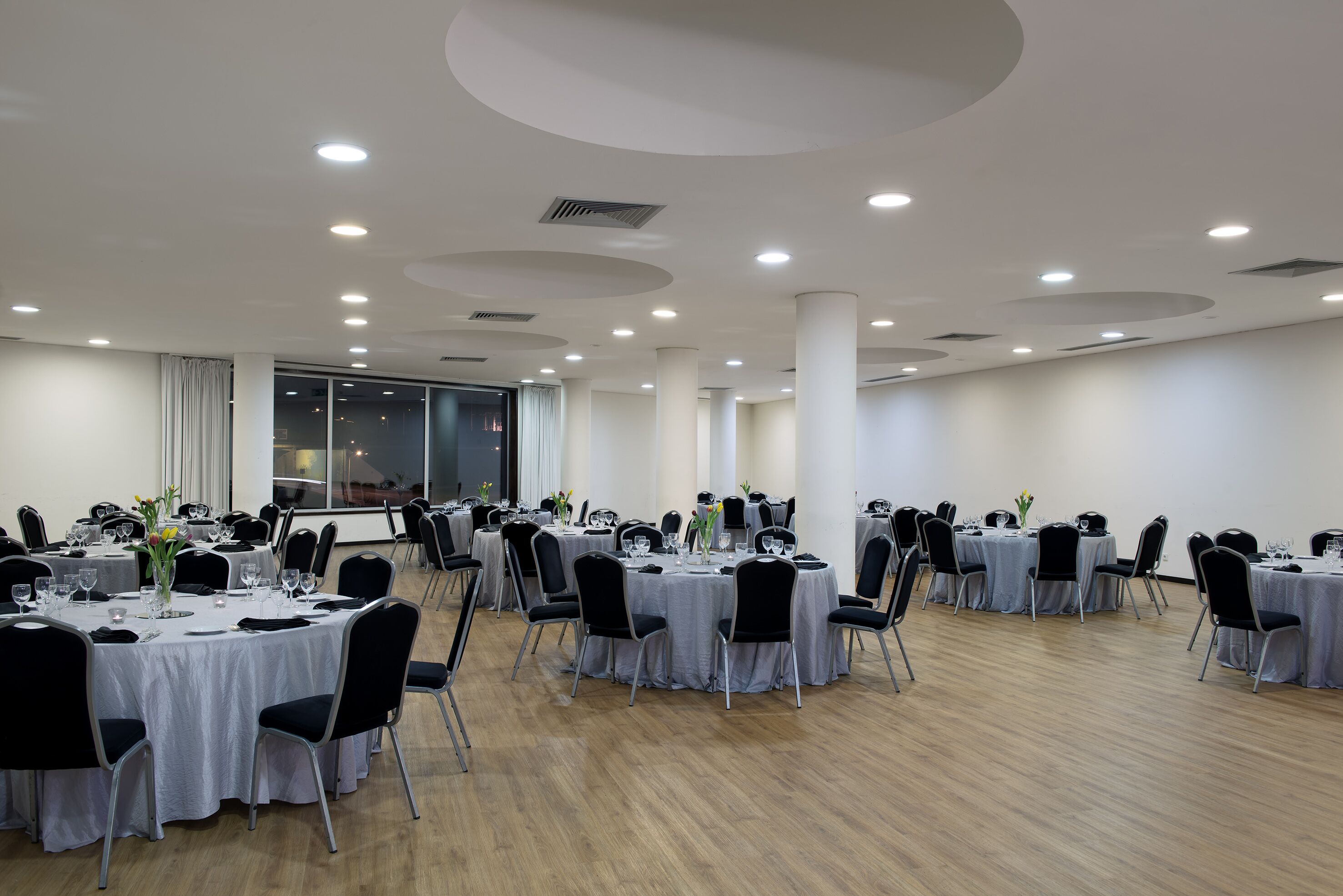 Une salle de conférence avec des tables rondes, des chaises noires et des nappes blanches.