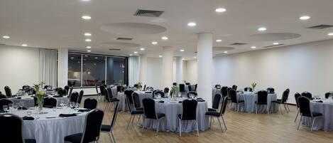 Une salle de conférence avec des tables rondes, des chaises noires et des nappes blanches.