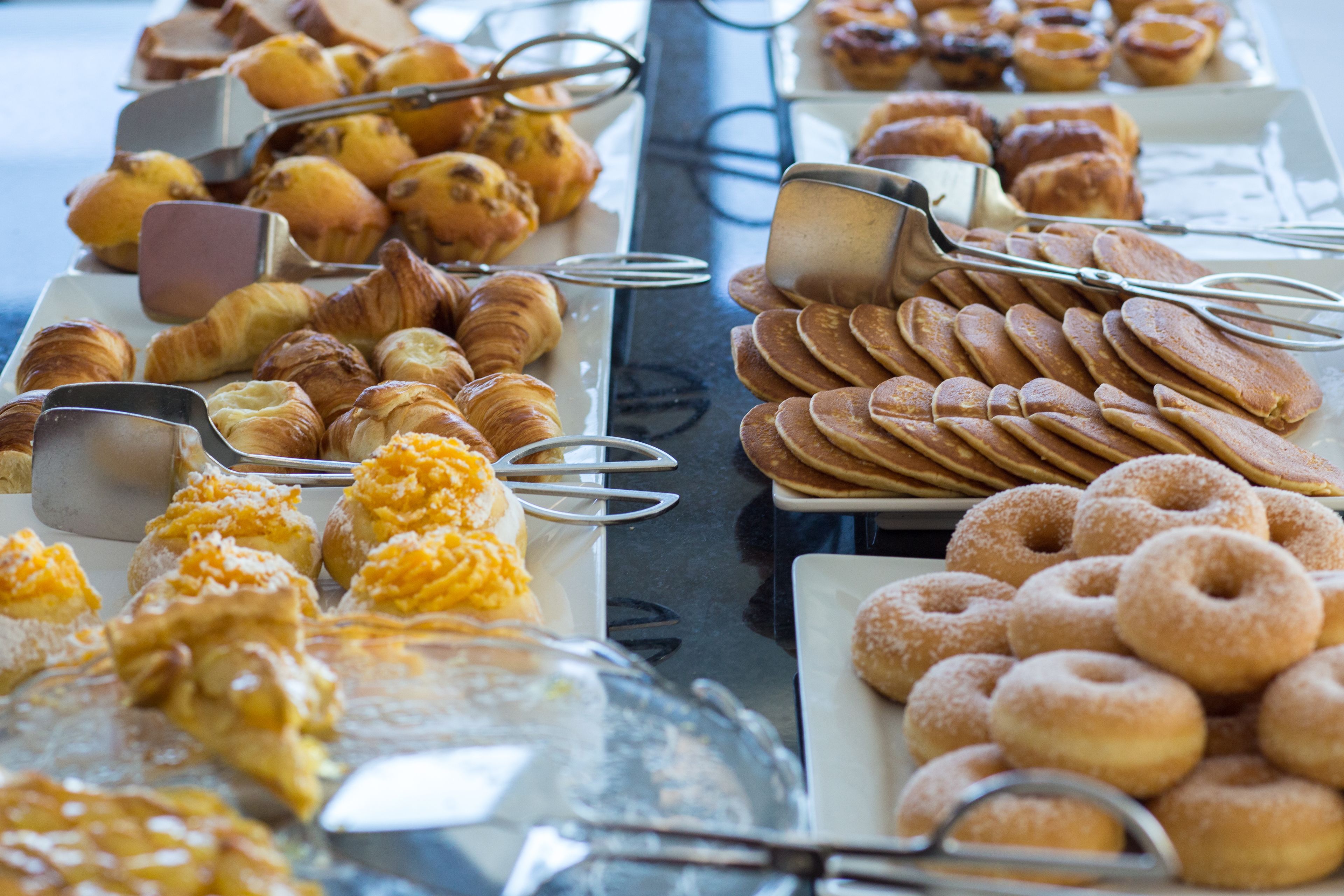 Ein Buffet mit verschiedenen Backwaren und Gebäck, darunter Croissants, Muffins und Donuts.