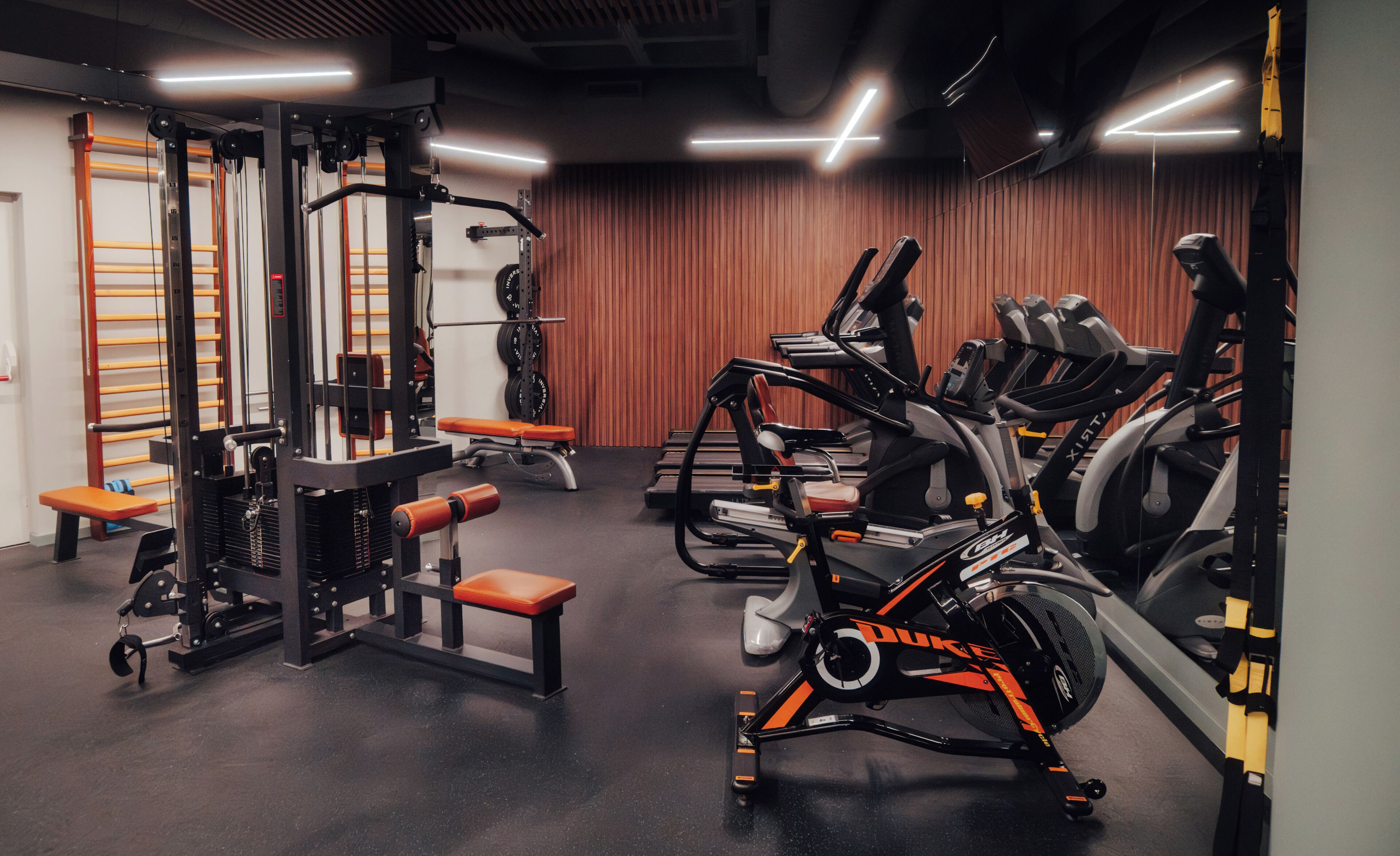 A gym with exercise equipment, benches, and a wall-mounted rack.