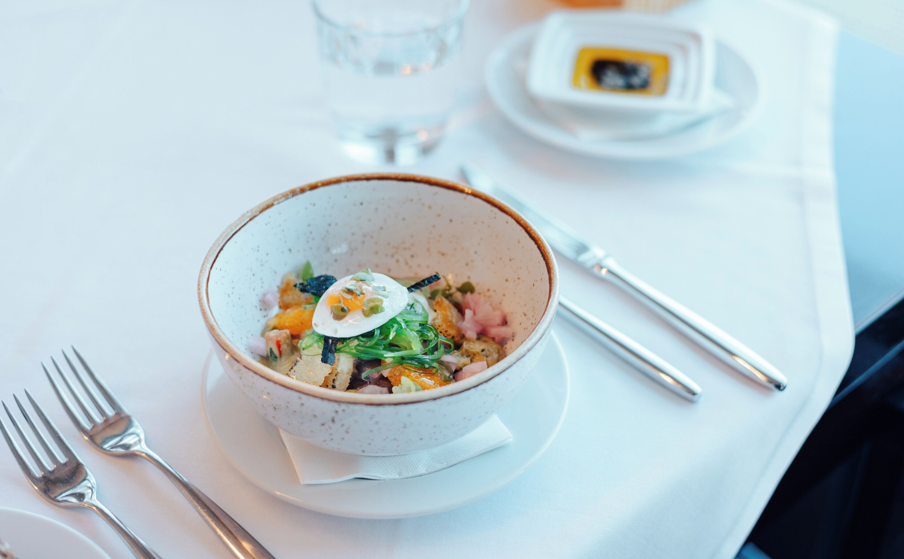 A bowl of food on a white table with a fork and a knife beside it.