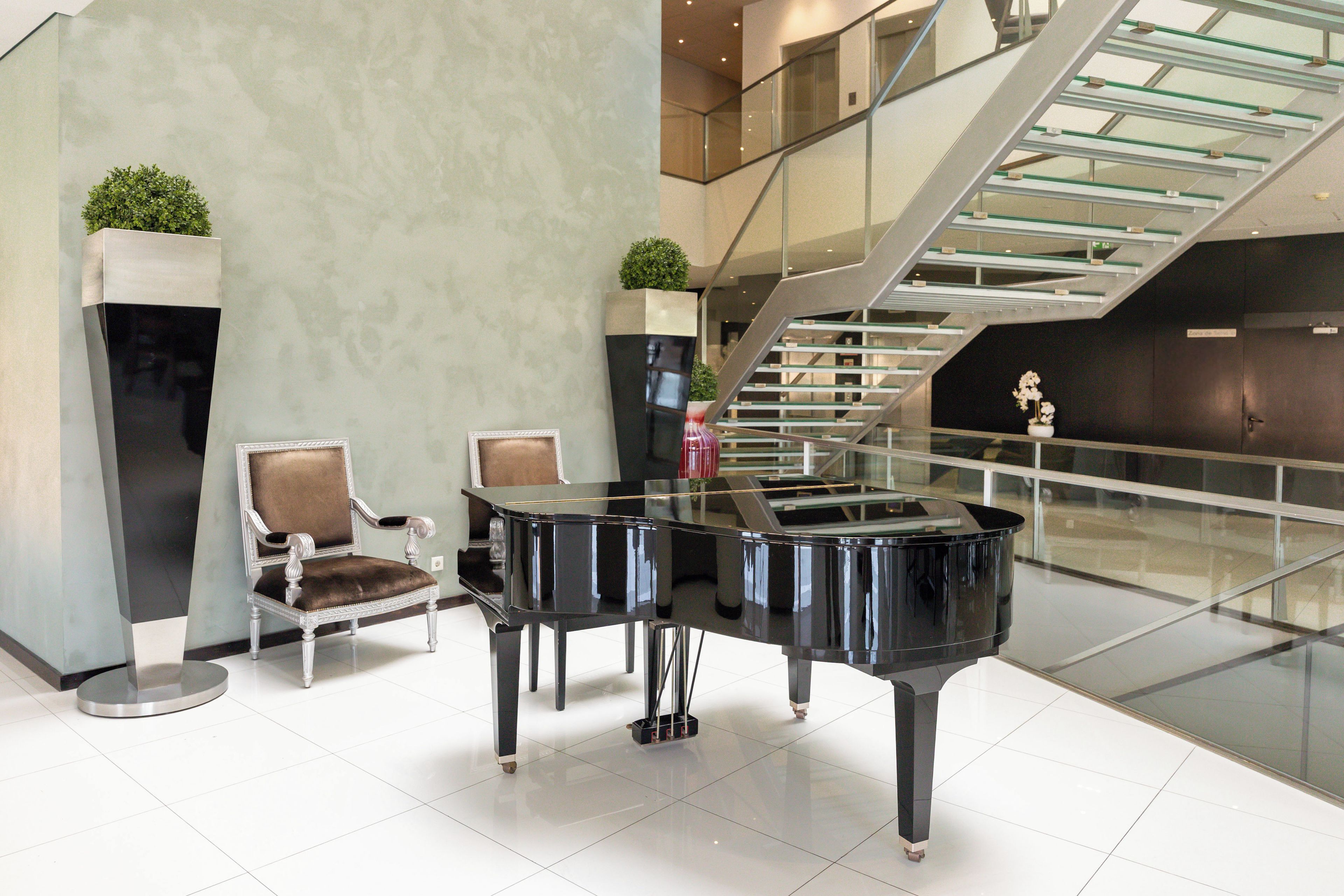 A grand piano in a spacious lobby with a staircase and a seating area.
